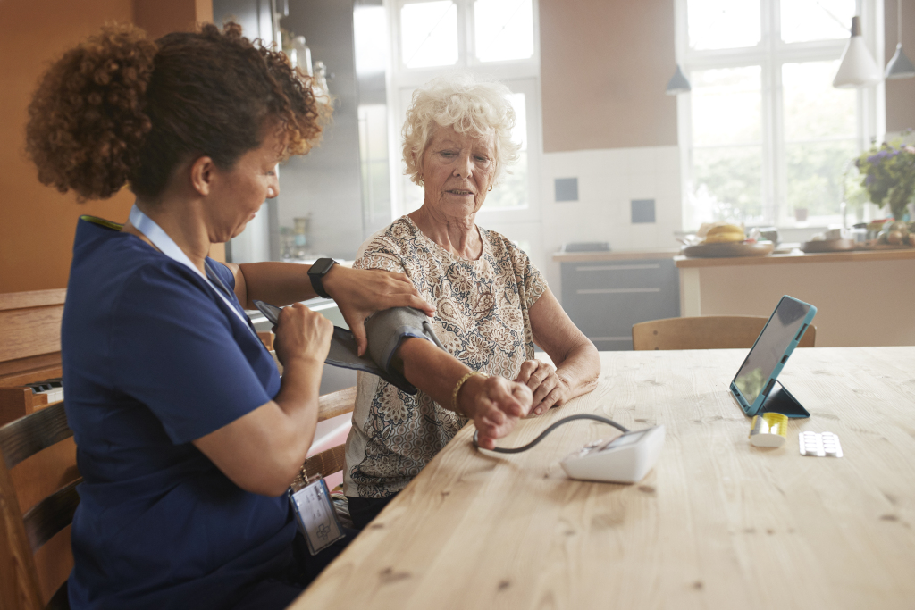 nurse measuring blood pressure of senior woman with gauge at table